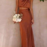 Luxurious silk satin skirt set featuring a high-waist maxi skirt and a backless halter top in rust color, size XL, worn by a model showcasing the elegant design with a joyful smile and styled hair.