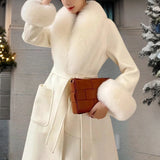 Luxury beige winter coat with faux fur collar, designed as a wool overcoat. Features include long sleeves, a stylish waistline, and a sophisticated trench coat style. Model is accessorized with a matching bag and gloves.