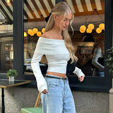 A woman standing in a stylish streetwear outfit, wearing a luxury black hair bow; she has jeans, a grey top with sleeves, and is accessorized with eyewear.