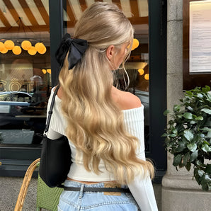 A stylish woman wearing a luxury black hair bow, complemented by a streetwear outfit featuring jeans and a yellow top with sleeves. She is accessorized with eyewear and the bow in her hair adds a fashionable touch to her overall look.