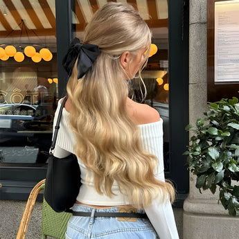A stylish woman wearing a luxury black hair bow, complemented by a streetwear outfit featuring jeans and a yellow top with sleeves. She is accessorized with eyewear and the bow in her hair adds a fashionable touch to her overall look.