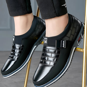 Black leather men's formal shoes with a designer checkered pattern, displayed on a model's feet.