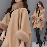 Luxurious women's camel wool cape with faux fur trim, showcasing elegant outerwear style, worn by a model with styled hair and fashionable shoes, highlighting winter fashion.
