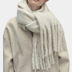 Elegant beige luxury cashmere scarf with fringe detailing, designed as a warm winter fashion accessory, draped around the neck like a shawl or stole.