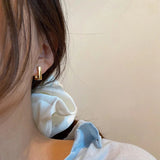 Close-up of a woman's ear wearing luxury gold geometric earrings in a modern minimalist stud design.