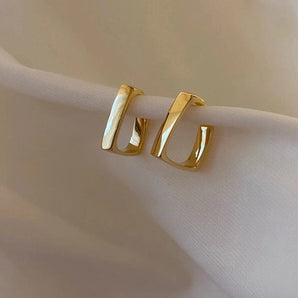 Luxury gold geometric earrings with a modern minimalist design on a beige background.