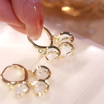 A pair of luxury gold hoop earrings with clear gemstone accents displayed in a vintage box, shown on a hand.