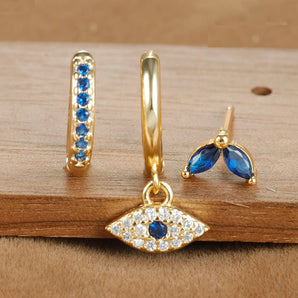 Luxury gold jewelry set featuring sapphire huggie earrings and an evil eye pendant, showcasing elegant gold craftsmanship with electric blue gemstones.