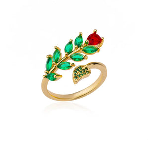 Luxury gold marquise ring featuring green emerald and red ruby accents in the shape of marquise and heart stones, displayed on a decorative background.