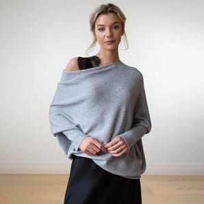 Luxurious light gray women's cashmere poncho draped elegantly on a model, showcasing its soft knit texture and flowing design, complete with a wide neckline and ample sleeves, exuding a sophisticated designer look.