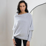 Luxury gray women's cashmere poncho draped elegantly over shoulders, showcasing the soft knit fabric and loose-fitting design. The poncho features a high collar and falls gracefully over the arms, providing a stylish and cozy appearance.