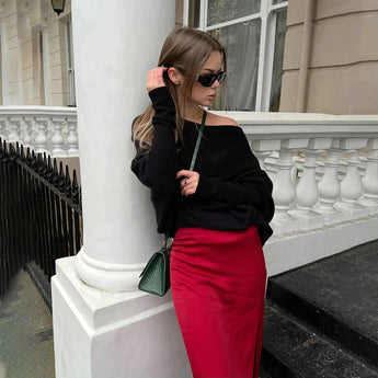 A woman wearing a luxury gray cashmere poncho stands with confidence, showcasing the elegant designer knitwear. The poncho drapes gracefully over her shoulders and arms, and she pairs the look with stylish sunglasses, adding a touch of sophistication to the fashionable ensemble.
