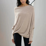 Luxury gray cashmere poncho worn by a woman, showing elegant designer knitwear with a focus on the neck, shoulder, and sleeves. The poncho is styled over a beige outfit, highlighting its versatile and sophisticated design.