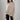 Luxury gray cashmere poncho worn by a woman, showing elegant designer knitwear with a focus on the neck, shoulder, and sleeves. The poncho is styled over a beige outfit, highlighting its versatile and sophisticated design.