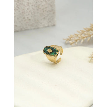 Luxury green gemstone ring with a textured 18K gold band by YA-CHAN, displayed on a beige background.