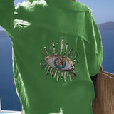 Luxurious green silk blouse with intricate sequin eye embellishment, featuring a stylish neckline and elegant sleeves.