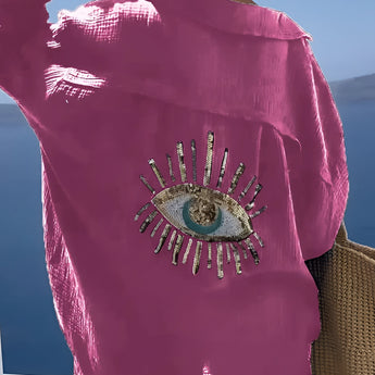 Luxurious pink silk blouse featuring a sequin eye embellishment on the front, designed with long sleeves and a stylish neckline.