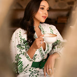 Luxury green and white embroidered maxi coat featuring floral patterns worn by a fashion model with black hair, showcasing the elegant garment's design with long sleeves and a maxi length, captured in flash photography.
