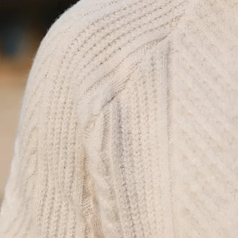 Luxury men's beige knit polo sweater featuring a woolen texture with long sleeves, paired with vintage pleated trousers. The image captures the intricate knit detail and elegant design of the ensemble.