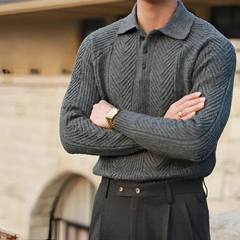 Luxury men's beige knit polo sweater paired with vintage pleated trousers, featuring a dress shirt with a collar and visible sleeve details. The image highlights elements of the upper body including the neck, shoulder, and arm, along with an accessory watch, all set against a subtle grey background.
