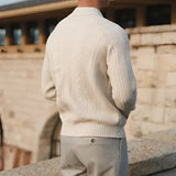 Luxury men's beige knit polo sweater paired with vintage pleated trousers, featuring a collared neckline and long sleeves, styled with a relaxed fit for a sophisticated look.
