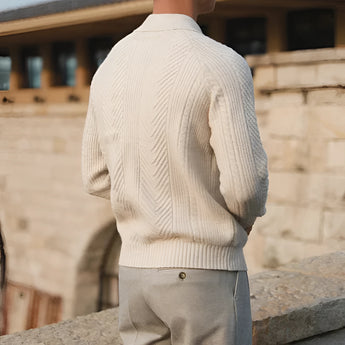 Luxury men's beige knit polo sweater paired with vintage pleated trousers, featuring a collared neckline and long sleeves, styled with a relaxed fit for a sophisticated look.