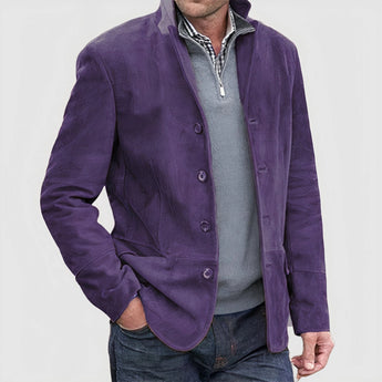 Luxury men's tan suede blazer in a single-breasted design, featuring a stylish purple inner lining. The model wearing the coat has a beard and is dressed in a grey dress shirt with a visible collar and sleeves.