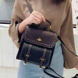 Luxury two-tone leather satchel with a studded flap, shown held by a hand and resting on the shoulder, highlighting its fashionable design and high-quality textile material.