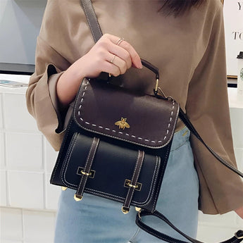 Luxury two-tone leather satchel with a studded flap, shown held by a hand and resting on the shoulder, highlighting its fashionable design and high-quality textile material.