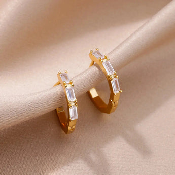 Luxury white gemstone gold hoop earrings for women displayed on a reflective surface.