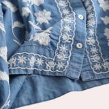 Luxurious women's denim top featuring floral embroidery, bell sleeves, and a button-up collar in an electric blue hue.
