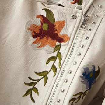 Luxury women's leather jacket featuring intricate floral and bird embroidery on the sleeves and body, showcasing detailed patterns of flowers, leaves, and petals, creating an artistic and elegant design.