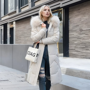 Luxury women's puffer coat with faux fur hood, featuring a grey color, stylish collar, and detailed sleeves, showcased in an urban setting near a window.