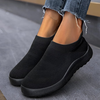 Magenta women's slip-on sneakers with a flexible sole, shown in nero color, worn by a person dressed in grey denim sportswear.
