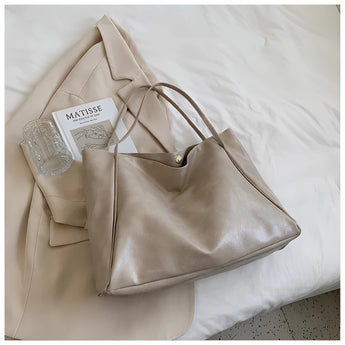 Beige leather tote bag with a minimalist design, featuring a large, rectangular shape and silver accents, suitable for use as a shoulder bag.