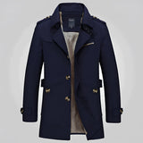 Men's beige double-breasted trench coat with epaulettes, featuring a classic collar and long sleeves, styled over a dress shirt for a formal and sophisticated look.