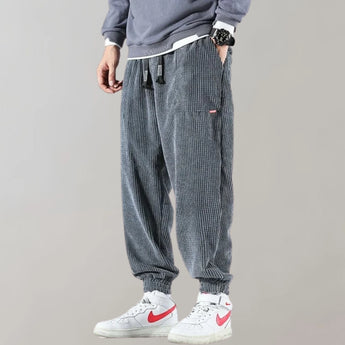 Men wearing light gray corduroy cargo pants with an ankle-tapered fit, paired with a white dress shirt and showcasing urban style.