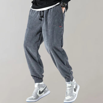 Men's black corduroy cargo pants featuring an ankle-tapered design, suitable for urban style. The pants have visible cargo pockets and a fitted waist, emphasizing both casual and sporty aesthetics.