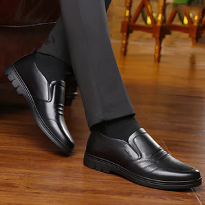 Men's black leather slip-on loafers on a wooden floor, showcasing a formal and comfortable design.