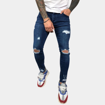 
A person wearing blue skinny jeans with ripped knees, showcasing an urban street style design. The jeans are made of denim fabric and fit snugly around the legs, highlighting the knee and thigh areas.