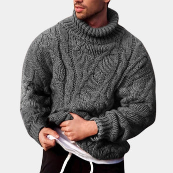 Men's gray wool cable knit turtleneck sweater featuring long sleeves and a high collar, worn by a bearded man.