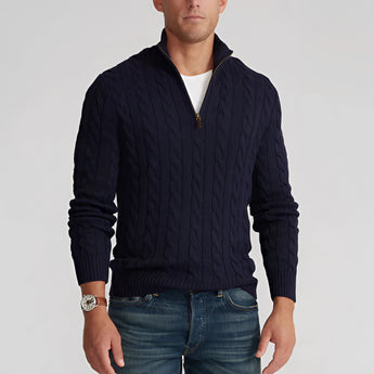 Men's blue cable knit zip-up sweater featuring ribbed trim details, worn by a model with the sweater partially unzipped to reveal a contrasting dress shirt underneath. The sweater showcases long sleeves and a high collar, suitable for winter fashion.