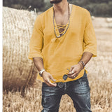 A man wearing a men's bohemian white hooded shirt with a lace-up neckline, paired with sunglasses, standing on grass under bright sunlight, smiling.