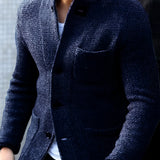 Men's charcoal tweed blazer in a slim fit design, featuring a classic herringbone pattern, modeled by an individual wearing a marine blue dress shirt underneath. The blazer has a structured collar, long sleeves, and is complemented by a watch on the wrist. The overall attire exudes a sophisticated and formal look.