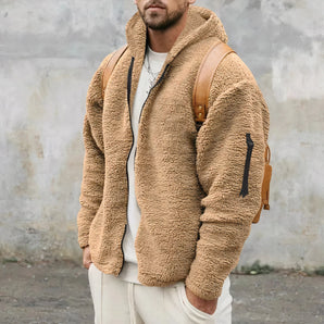 Men's fluffy teddy bear jacket in camel color, featuring a fleece-lined hoodie. The jacket appears to be worn by a model with a beard, showcasing details like the neck, sleeve, and collar in the image. The overall design suggests a cozy and warm garment suitable for fashion-conscious individuals.