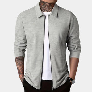 Men's gray slim fit blazer designed for casual wear, featuring a lightweight and urban style. The image shows the blazer being worn over a white dress shirt. The blazer has a sleek collar and long sleeves.