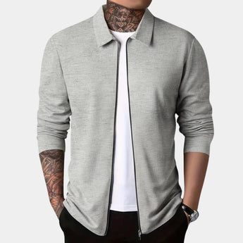 Men's gray slim fit blazer designed for casual wear, featuring a lightweight and urban style. The image shows the blazer being worn over a white dress shirt. The blazer has a sleek collar and long sleeves.