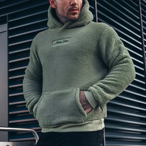 Men's green fleece teddy hoodie in an urban streetwear style, featuring a warm woolen texture, long sleeves, and a cozy collar. The model stands showcasing the 2XL size, complemented by a beard.