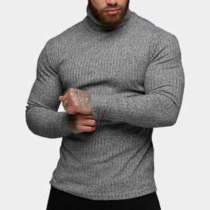 Men's grey knit turtleneck sweater with a fitted muscle fit design, showcasing long sleeves, a high collar, and a textured textile, worn by a bearded model.