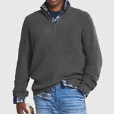 Men's grey ribbed half-zip sweater shown worn over a white dress shirt, paired with jeans. The sweater is a part of fall and winter knitwear collection, designed for comfort and style. Model with a beard wears the sweater, which features a ribbed texture and extended sleeves, suitable for casual or semi-formal occasions.